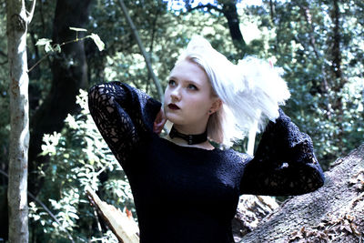 Woman looking away while standing against trees