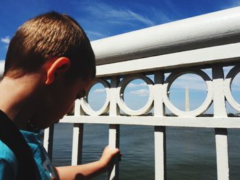 Close-up portrait of boy on railing against sky