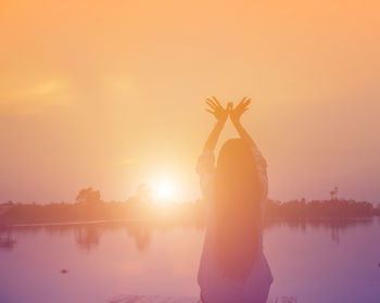 Rear view of woman standing in lake against sky during sunset