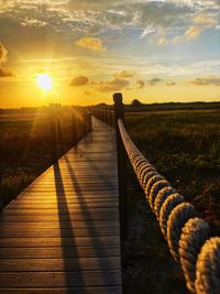 Wooden footbridge against sky during sunset