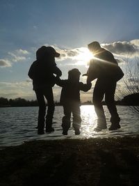 Silhouette of people standing in water at sunset