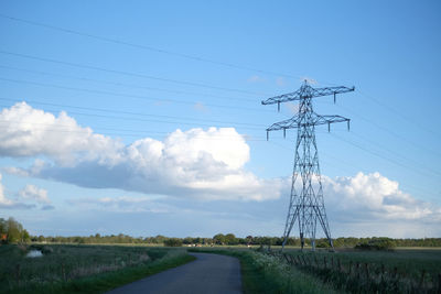 Electricity pylon on road amidst field against sky