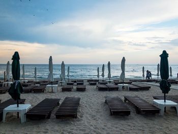 A beach with empty sunbeds and closed umbrellas on a day with dark storm clouds