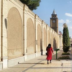 Rear view of woman walking on footpath by retaining wall in city