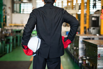 Rear view of man wearing suit and glove standing in factory