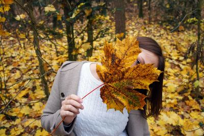 Low section of woman holding autumn leaves in forest