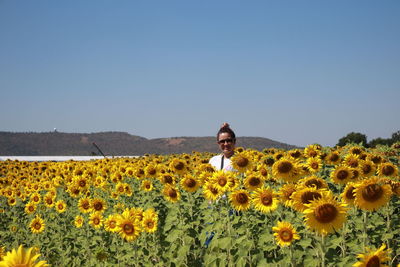 Portrait of smiling woman standing amidst sunflowers on field against clear sky