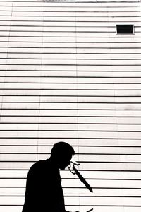 Side view of silhouette man holding umbrella against wall