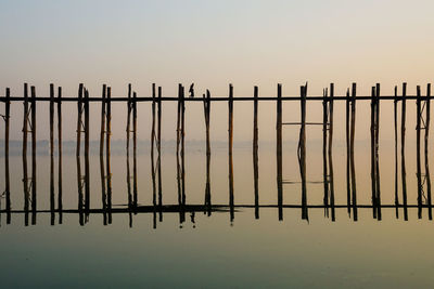 Silhouette fence by wooden post against sky during sunset