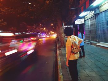 Rear view of woman walking on illuminated street at night