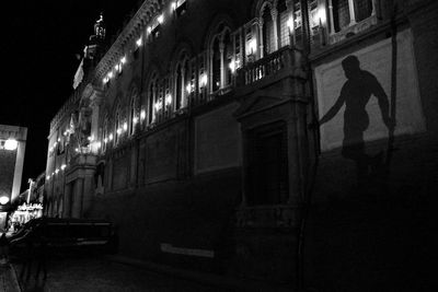 Man walking on illuminated street amidst buildings in city at night