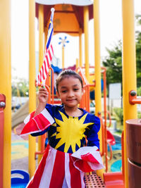 Portrait of smiling girl holding malaysian flag on jungle gym at playground