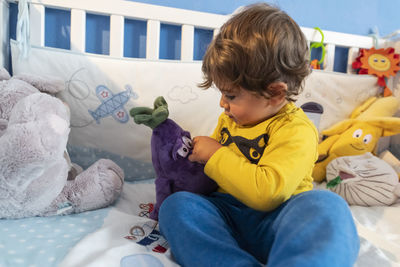 Toddler plays in cot with cuddly toy. person