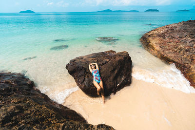 Young woman on rock at beach against sky