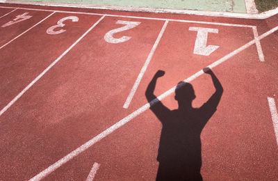 Shadow of athlete with arms raised standing on running track