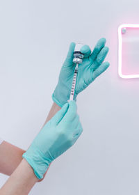 Cropped hands of doctor holding syringe and vial against wall