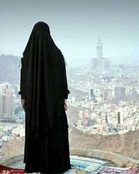 Rear view of man looking at city buildings against sky