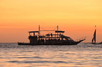 Silhouette ship in sea against orange sky