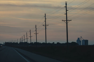 Silhouette electricity pylons against sky during sunset