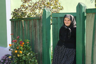 Young woman standing in front of wooden fence against plants
