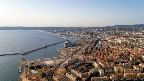 Aerial view of cityscape by sea against clear sky during sunset