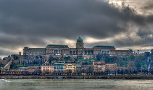 Buildings at waterfront against cloudy sky