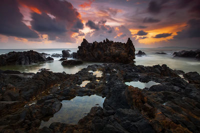 Rock formation on beach against sky during sunset