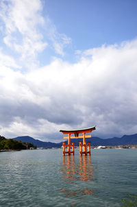 Torii gate in sea at itsukushima shrine against sky