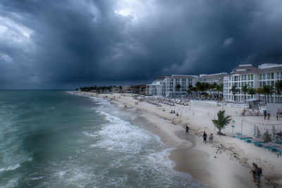 View of people on beach against storm clouds