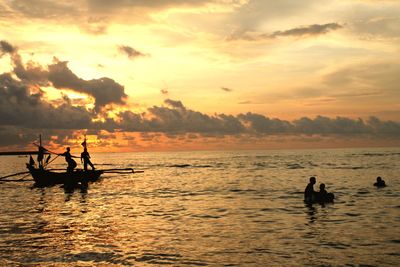 Silhouette people in sea against sky during sunset