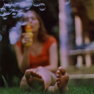 Full length of young woman blowing bubbles while sitting in back yard