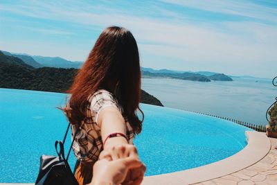 Woman holding hand of person by swimming pool against sky