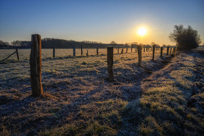 Wooden posts on field against sky during sunset