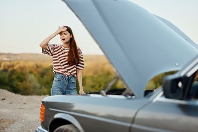 Portrait of smiling friends using mobile phone while standing against car