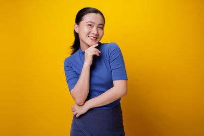 Portrait of smiling young woman against yellow background