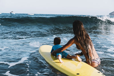 Back view of mother and son on a surfboard at sea