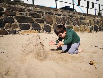 Full length of boy throwing sand while playing at beach