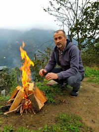 Portrait of man crouching by campfire