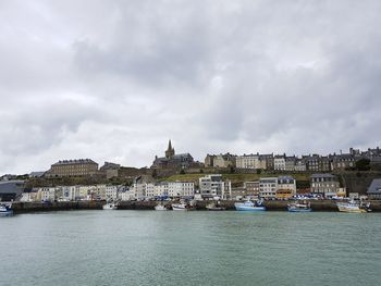 City at waterfront against cloudy sky