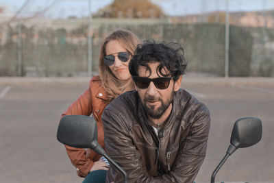 Portrait of man and woman sitting on motorcycle in city