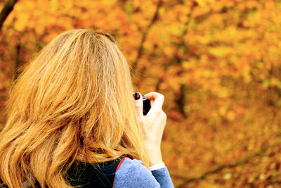 Rear view of mature woman photographing autumn trees at park