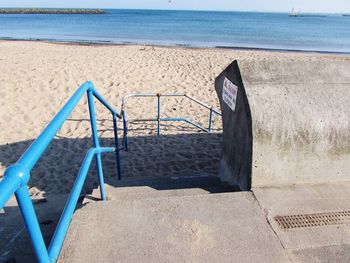 Shadow of railing on beach against sky