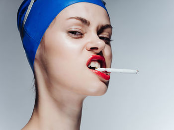 Close-up portrait of woman smoking cigarette against white background