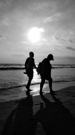 Silhouette people on beach against sky during sunset