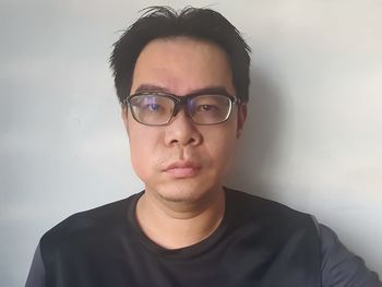 Portrait of young man wearing eyeglasses against wall