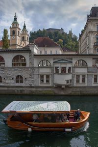 Boats in river by buildings against sky