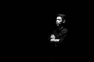 Portrait of young man standing against black background