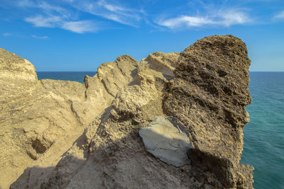 Rocks on shore by sea against blue sky