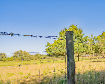 Fence on field against clear blue sky