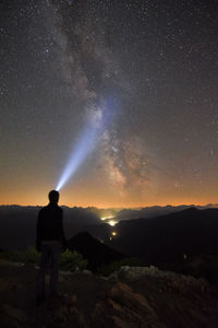 Rear view of man looking at mountains against sky at night